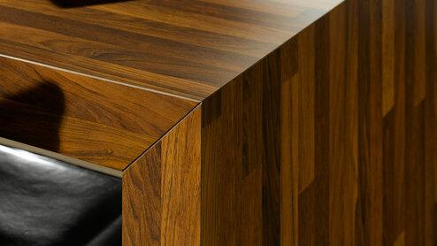 Detailaufnahme eines Esstisches aus dunklem Massivholz in Kombination mit Ledersessel