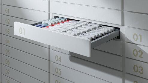 Detailaufnahme von schmalen weißen Medikamentenschubläden mit dezenter Nummerierung und sichtbarer Medikamentenaufteilungen.