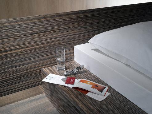 Detailaufnahme von Bettumrandung in dunklem Holz mit Ablagemöglichkeit